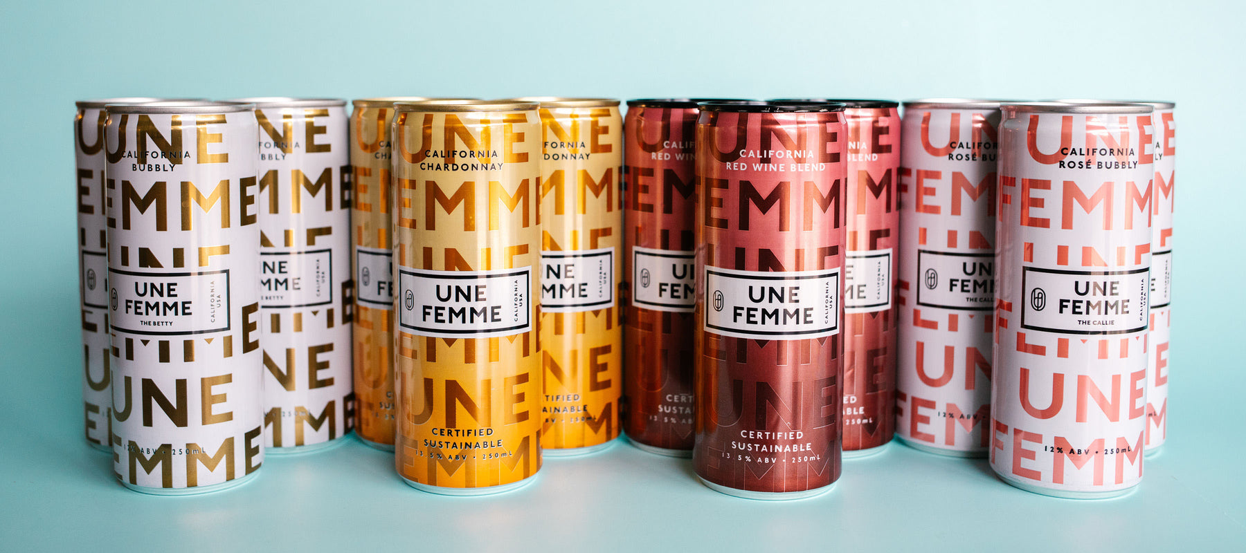 A collection of Une Femme cans with various metallic colors, including gold, copper, and rose. The background is a soft teal color.